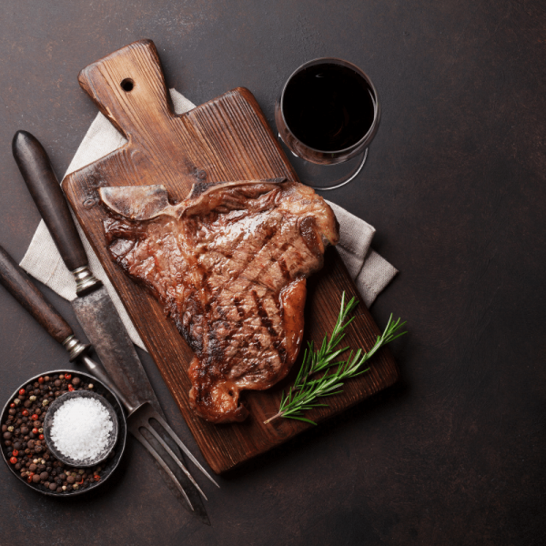t-bone steak on table with wine cutlery and herbs